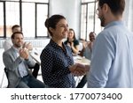 Small photo of Happy proud excited Indian ethnicity employee get promotion receive praises from boss and cheering and congratulations from diverse staff members shake hands with chief. Recognition of success concept