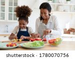 Smiling young african American mother and small daughter chop vegetables prepare healthy vegetarian salad in kitchen, happy biracial mom teach little girl child cooking food at home, dieting concept