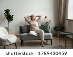 In light living room on modern comfy couch rest aged woman, grandma closed eyes enjoy peace and placidity, put hands behind head breath fresh humidifier air. No stress, carefree retired life concept
