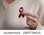 Close up mature woman holding red awareness ribbon in hand, middle aged female supporting people with disease, regular checkup promotion, symbol of fight against AID, HIV, cancer, drugs addiction