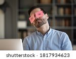Small photo of Exhausted young Caucasian man worker have sticker pads on eyes sleeping near computer in office. Tired millennial male employee fall asleep doze off at workplace, feel overwhelmed drained at work.