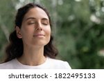 Close up of happy young Caucasian woman isolated on blurred background dream visualize with eyes closed. Smiling dreamy female breathe fresh air relieve negative emotions. Stress free concept.
