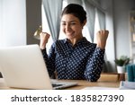 Overjoyed indian ethnicity girl sit at desk looks at laptop screen read incredible news clench fists makes yes gesture celebrate on-line lottery gambling win, getting new job offer feels happy concept