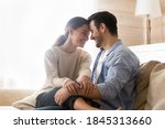 Happy together. Smiling newlyweds cuddling on couch at living room of rented purchased flat, caring husband hugging holding on knees beloved wife, young couple is glad to start new independent life