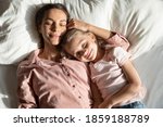 Calm mother with little 6s 7s daughter sleeping together lying down on pillow in comfortable bed, caring mom and lovely kid, top above view. Healthy nap at daytime, repose, relaxation moment concept