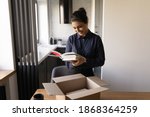 Small photo of Happy millennial female of indian ethnicity preparing moving relocation to new home packing things. Glad proud young hindu woman author get parcel with personal copies of book from publishing house