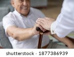 Small photo of Close up of nurse caregiver palms covering hand of smiling senior patient holding cane. Sick old man struggle with trauma consequence make success on rehabilitation therapy with help support of doctor