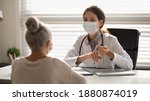 Female doctor in medical facial mask have consultation with elderly patient during covid-19 pandemics. Woman GP in facemask talk consult mature client in clinic or hospital. Coronavirus concept.