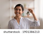 Small photo of House of dream. Headshot portrait of excited indian female happy winner buyer renter tenant of new home apartment. Young mixed race woman proud homeowner looking at camera showing keys of modern flat