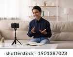 Small photo of Indian female popular video blogger shoot video content at home make topical review before webcam of phone fixed on tripod. Young hindu lady coach talk on camera of cell device broadcast speech online