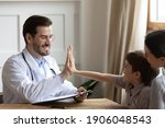 Small photo of Happy young Caucasian male doctor give high five to cute small 7s boy patient at consultation with mom in hospital. Smiling pediatrician make deal cheer little kid child in clinic. Healthcare concept.