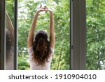 Meeting summer day. Back rear view of happy young woman stand in balcony door stretch hands enjoy weekend have pleasure. Calm beautiful female do morning exercises practice yoga by opened large window