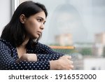 Small photo of Profile of stressed young asian lady sitting on sill by window think hesitate unable to make choice in hard situation. Suffering teen vietnamese female with depressed look has life crisis. Copy space