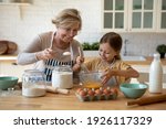 Cooking with soul. Happy little girl in apron help senior grandma at kitchen mix dough for cookies pancakes. Smiling older granny teach small grandkid to bake homemade cake pastry share family recipe