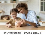Small photo of Setting good example. Young parent mother teach child little daughter girl to manage finances save money spend earnings with economy plan family budget. Friendly mom and kid thrift coins in piggybank