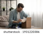 Small photo of Present from distant friend. Happy millennial man unpack open box with birthday gift surprise received by mail. Smiling young guy has pleasure to receive package with consumer goods purchased online