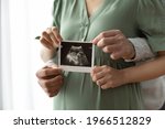 Crop close up of happy young multiethnic future parents hold ultrasound picture of baby. Diverse man and pregnant woman show sonogram image on kid child, excited for parenthood. Parenting concept.
