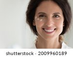 Small photo of Close up portrait of smiling young latin female face with cosmetic cream moisturizer drops on skin under eyes. Happy millennial lady look at camera introduce new antiage creme serum lotion. Copy space
