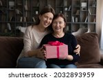 Portrait of smiling affectionate young woman cuddling sincere joyful elder mature retired mother holding wrapped box with present gift in hands, happy birthday or special event celebration concept.