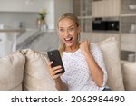 Small photo of Overjoyed sincere young woman holding telephone, feeling festive getting online lottery win notification, celebrating internet success giveaway betting auction win alone at home, reaction of happiness