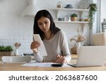 Small photo of Serious young Asian woman, renter, homeowner checking, calculating utility bill, seeing mistaken too high costs, looking at paper receipt with doubt, having problems with mortgage, taxes fee payment
