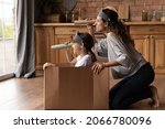 Small photo of Happy creative mother and active daughter girl playing pirates ship at home, sailing carton box boat, looking forward through toy paper spyglasses, enjoying home activities. Family role game