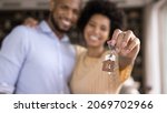 Small photo of Close up focus on keys in hands of blurred joyful young loving african american married couple. Sincere mixed race homeowners celebrating purchasing own flat, feeling excited of renting new dwelling.