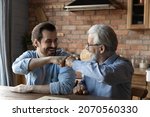Small photo of Friendly draw. Happy joyful two men of different age give fist bump after ending game of checkers draughts. Laughing elderly father retiree and millennial son greet each other with finishing boardgame