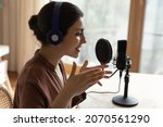 Female podcaster sit at table speaking into microphone stand on tripod talk speech share information, make audio podcast for internet audience, close up. Streaming, online radio program event concept