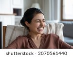 Small photo of Close up image of laughing young Indian ethnicity woman sit on armchair giggling on funny movie or anecdote enjoy humor stand up tv show. Jokes, pranks, happy face expression, candid emotions concept