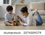 Small photo of Happy Indian mom and little son playing motor mechanic games with on heating floor, repairing toy plastic car with screwdrivers. Father and kid enjoying playtime, development activities at home