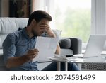 Small photo of Depressed unhappy young man covering eyes holding paper document, feeling stressed of getting dismissal notice or bank debt notification, having lack of money financial problems, bankruptcy concept.