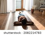Relaxed happy young indian ethnicity woman homeowner lying alone on warm wooden floor with underfloor heating, enjoying carefree peaceful weekend leisure time alone in modern stylish living room.