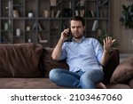 Small photo of Angry dissatisfied man talking on phone, arguing or solving problem, sitting on couch at home, irritated unhappy client having unpleasant conversation with customer support service, complaining