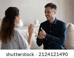 Small photo of Smiling man and woman with deafness using signs for communication, sitting on couch at home, smiling. Therapist teaching gesture language to patient with disability. Hearing disorder concept