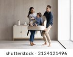 Couple of happy funny parents holding cheerful little son sat in armchair. Family moving into new house, carrying furniture, feeling joy. Mom and dad playing active games with kid. Relocation concept