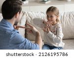 Small photo of Happy pretty daughter kid and father talking with gestures, speaking sign language at home. Therapist training smiling child with hearing disability, deafness to use hands, fingers for communication
