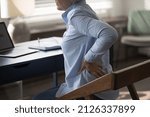Small photo of Cropped unhealthy middle aged senior woman employee massaging stiff back muscles, suffering from sudden pain, sitting at table doing computer work, feeling strong lumbar ache at modern home office.