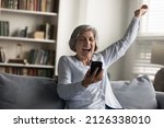 Small photo of Overjoyed old middle aged 50s woman making yes gesture laughing, looking at cellphone screen, getting message or email with unbelievable news, celebrating online lottery gambling giveaway win.