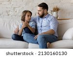 Serious father listen to his pre-teen little son talking seated on sofa at home, speaking spend time together at home. Cute boy share problems, ask advice to dad. Communication, care and trust concept