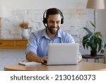 Smiling handsome young man wear headset sit in front of laptop, e-learns, take part in online study use modern tech, video conference application. Business, get new knowledge through internet concept