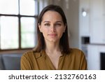 Small photo of Head shot beautiful young 30s female standing in fashionable living room alone pose looking at camera. Homeowner or apartment renter person, pretty housewife portrait, natural womens beauty concept
