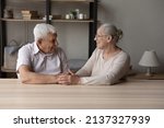 Small photo of Happy marriage, eternal love, trustworthy harmonic relations between older spouses concept. Senior grandparents sit at table at home smile look at each other hold hands feel endearment, express caress