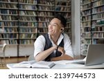 Small photo of Excellent student, effective e-learn, higher education, professionals skills concept. Handsome Asian guy sit at table in library, distracted from study, prepare for exams, make assignment looks aside