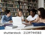African student guy with schoolmates sit at table in library discuss collaborative task. Multi ethnic schoolgirls schoolboys learn subject, studying together, gain knowledge, prepare for exams concept