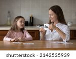 Small photo of Daycare teacher and little kid girl learning math, working with multiplication table, using flash cards, playing educational game. Mom helping daughter kid with mathematic school task