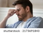 Small photo of Overworked at computer. Tired exhausted millennial male employee businessman freelancer frowning rubbing bridge of nose suffering of eye pain dizziness blurry vision sudden headache or migraine attack