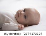 Small photo of Close up shot cute newborn baby in bodysuit lying down alone on bed. Adorable infant rests on white bedsheets, staring at camera looking peaceful. Infancy, healthcare and paediatrics, babyhood concept