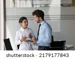 Two engaged diverse managers in formal clothed discussing business project, talking in office, using tablet computer. Indian female boss, manager training new employee, intern