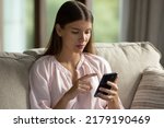 Small photo of Young beautiful woman sit on sofa in living room using modern smartphone, make call or order at home. Client of e-commerce services, mobile application usage. Technology, connection, lifestyle concept